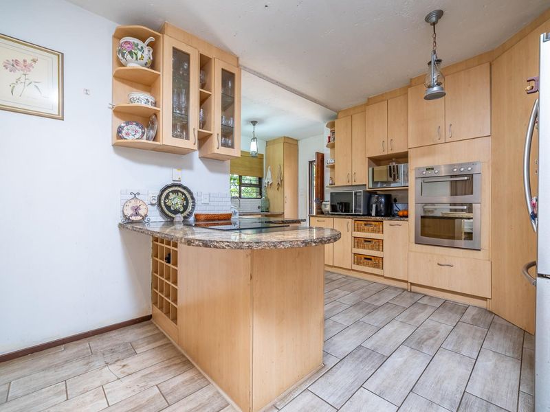 A functional kitchen featuring light wood cabinetry, granite countertops, a built-in oven, and a breakfast bar with an integrated wine rack.