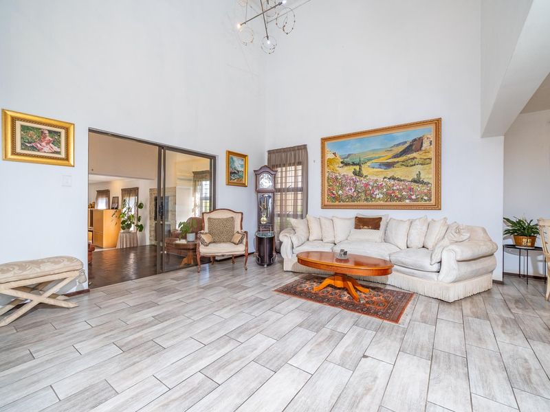 Spacious living room featuring high vaulted ceilings, modern wood-look tile flooring, and large sliding glass doors leading to an adjacent room.
