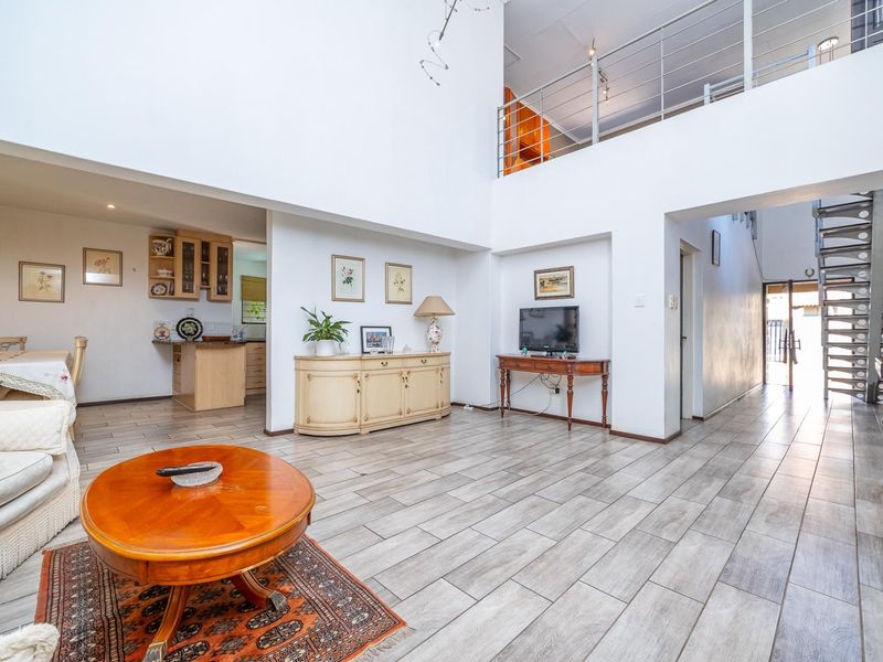 Spacious open-plan living area featuring double volume ceilings, tiled flooring, and a modern metal staircase leading to a mezzanine level.