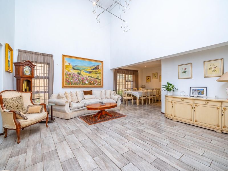 Spacious open-plan living and dining area featuring high double-volume ceilings, modern wood-look tiled flooring, and abundant natural light through large windows.