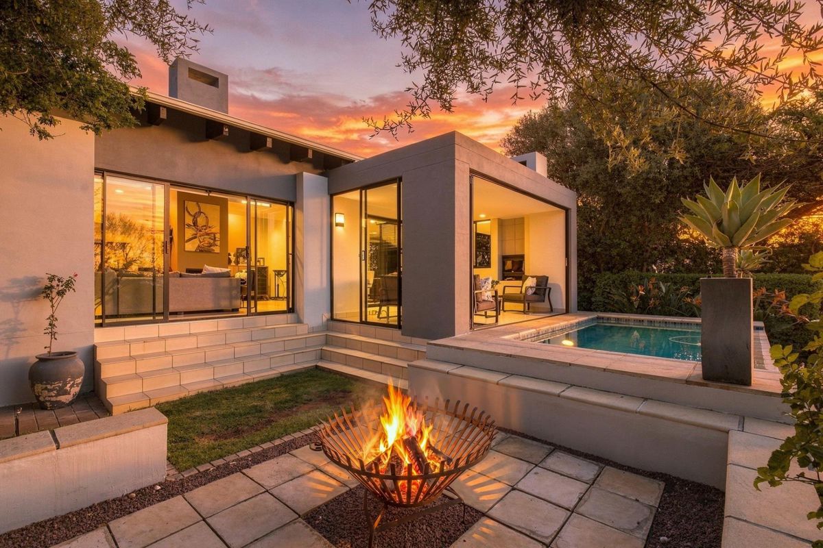 A beautifully landscaped rear exterior featuring a modern swimming pool, paved patio area, and seamless indoor-outdoor flow through large sliding glass doors.