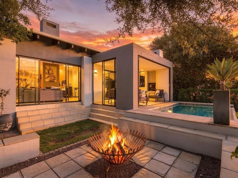 A beautifully landscaped rear exterior featuring a modern swimming pool, paved patio area, and seamless indoor-outdoor flow through large sliding glass doors.