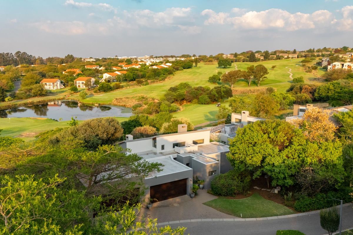 Aerial view of a modern residential property situated on a golf estate, featuring a paved driveway, garage, and scenic views of the surrounding landscape.