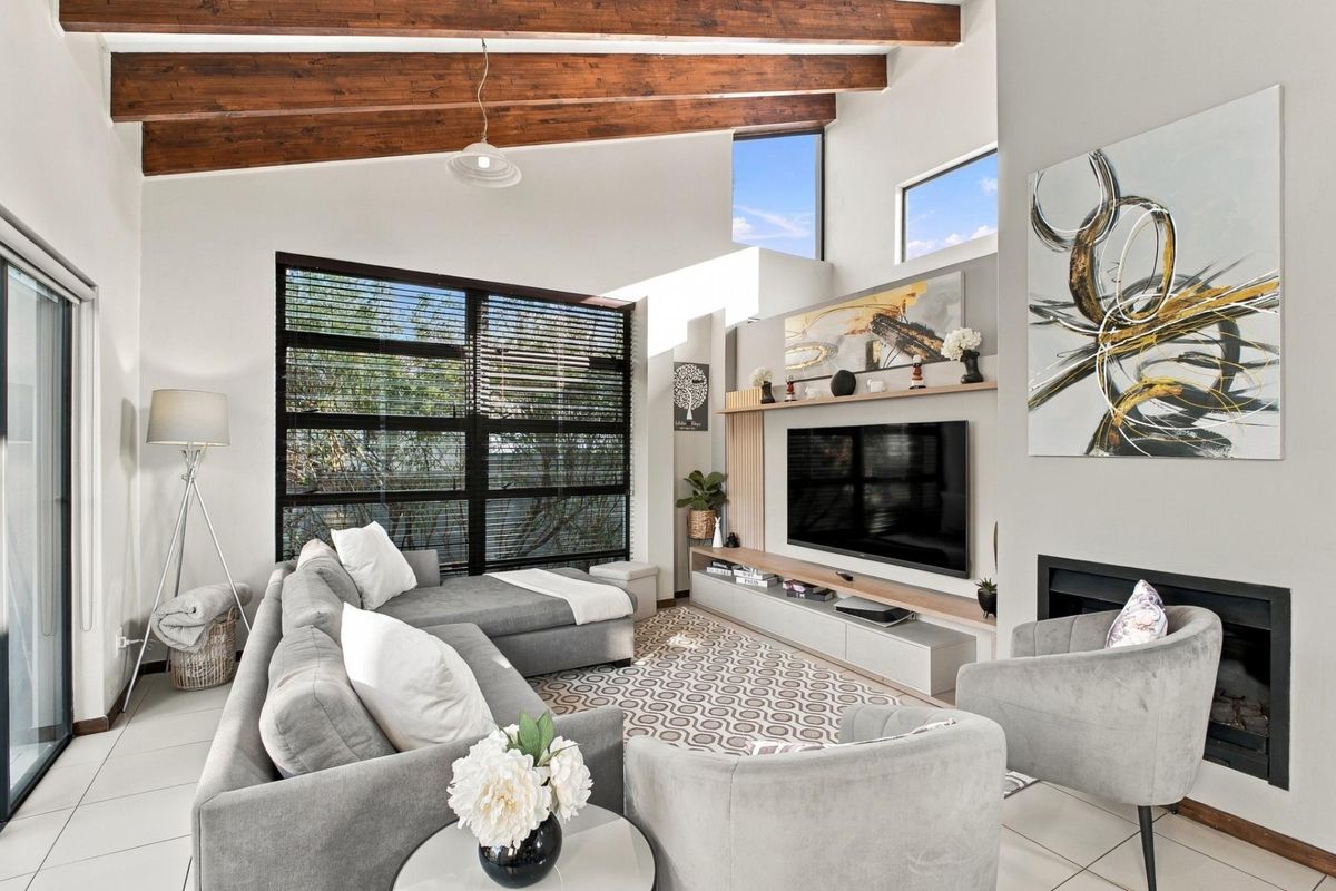 Modern living room featuring high vaulted ceilings with exposed timber beams, a built-in media unit, fireplace, and large windows providing ample natural light.