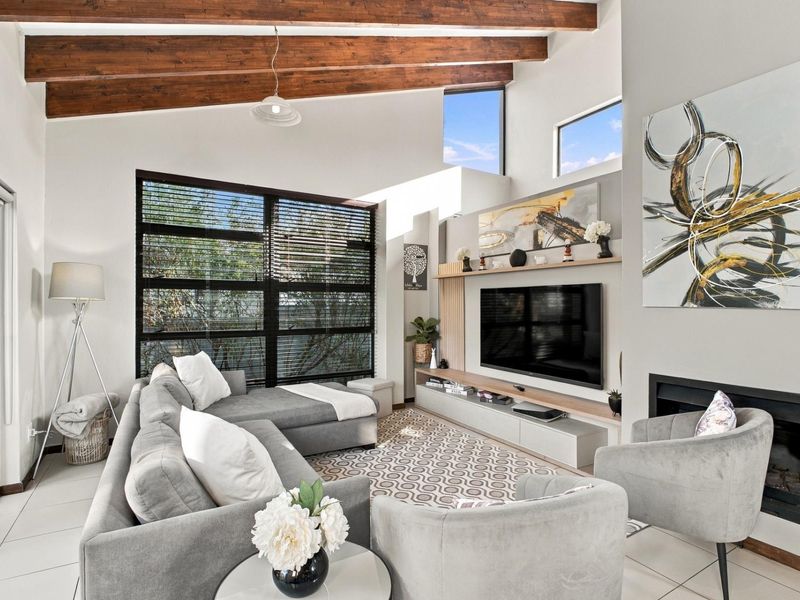 Modern living room featuring high vaulted ceilings with exposed timber beams, a built-in media unit, fireplace, and large windows providing ample natural light.
