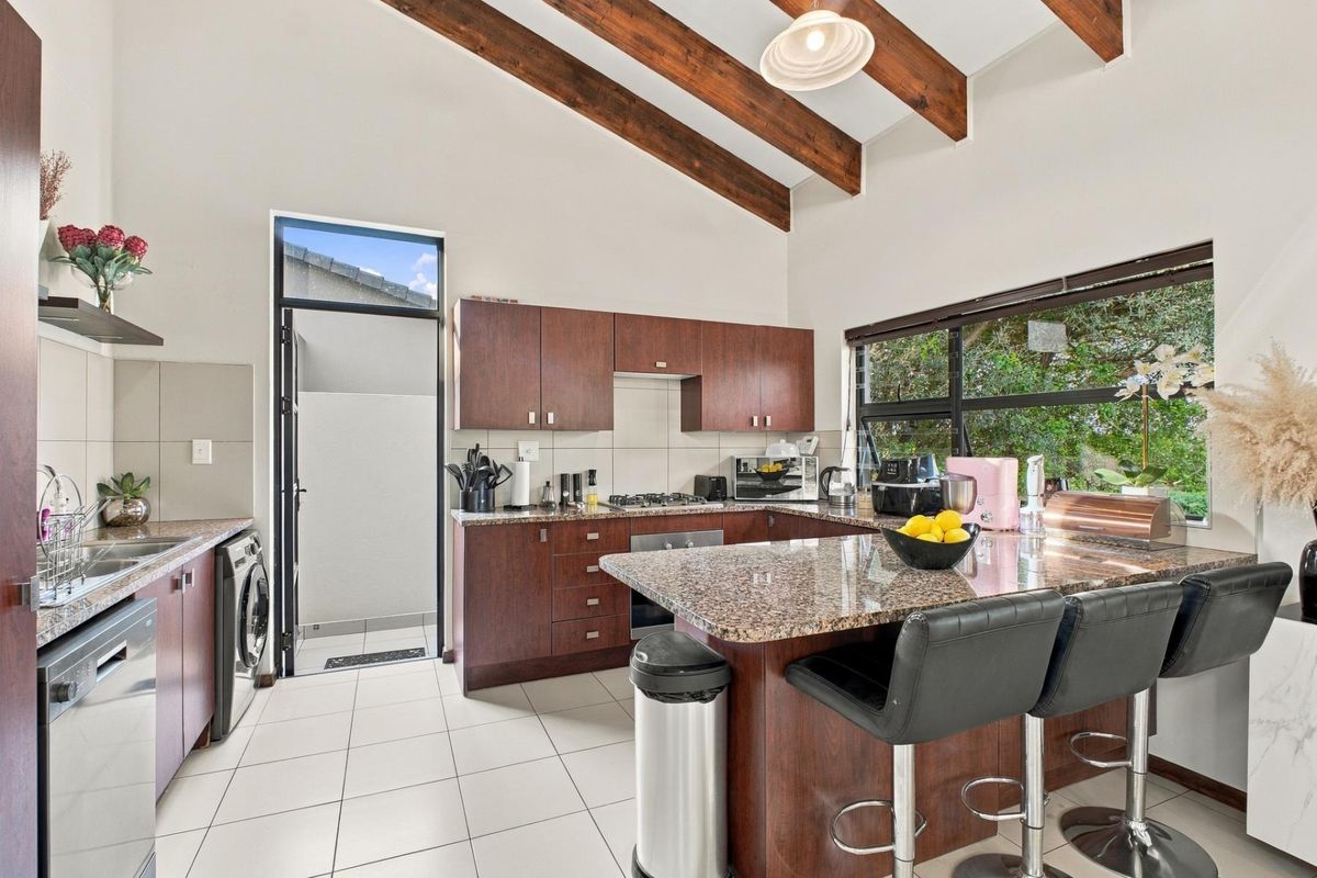 Spacious kitchen featuring granite countertops, dark wood cabinetry, exposed timber ceiling beams, and large windows providing ample natural light.
