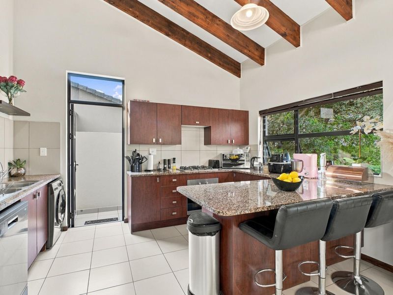 Spacious kitchen featuring granite countertops, dark wood cabinetry, exposed timber ceiling beams, and large windows providing ample natural light.