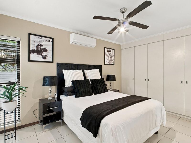 A well-maintained bedroom featuring tiled flooring, built-in cupboards, a ceiling fan, and a wall-mounted split-system air conditioner.
