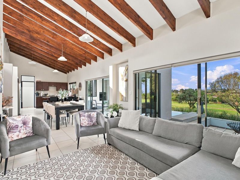 Spacious open-plan living and dining area featuring high vaulted ceilings with exposed timber beams, tiled floors, and large sliding doors opening to the garden.