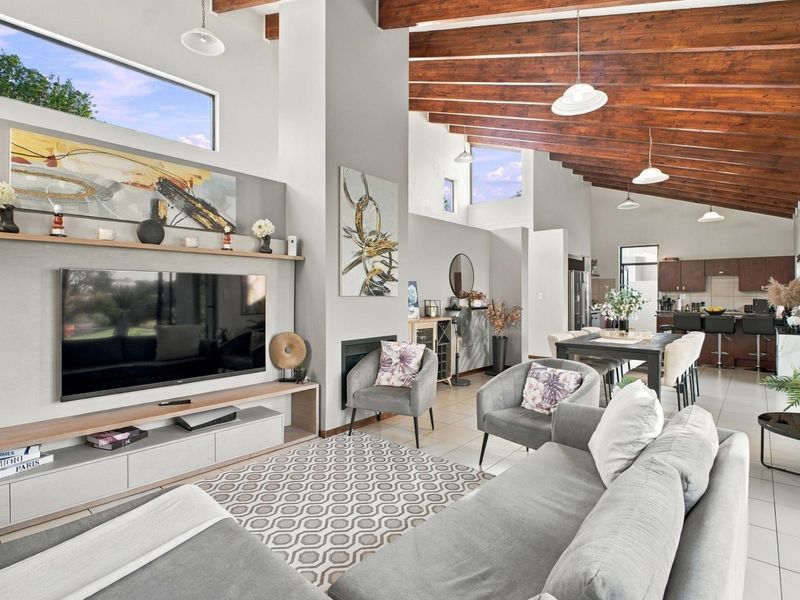 Spacious open-plan living and dining area featuring high vaulted ceilings with exposed timber beams, a modern fireplace, and a sleek integrated kitchen.