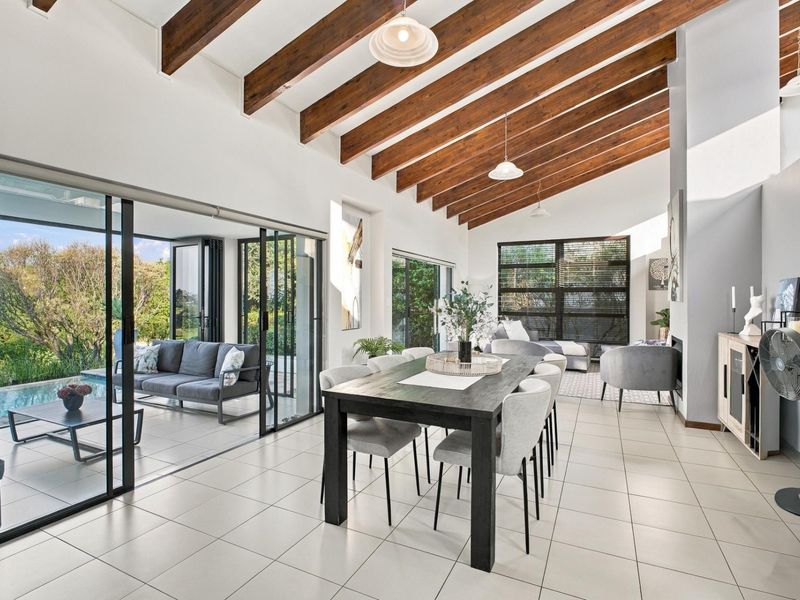 Spacious open-plan living and dining area featuring exposed timber beams, tiled floors, and large sliding doors opening to a patio and pool area.