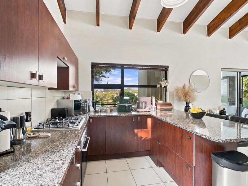 Modern kitchen featuring granite countertops, built-in gas hob, oven, and exposed timber ceiling beams, offering a functional workspace with natural light.