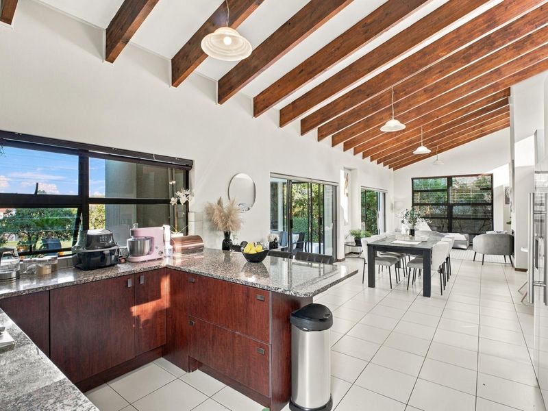 Spacious open-plan living and kitchen area featuring exposed timber ceiling beams, granite countertops, and large sliding doors leading to the outdoor space.