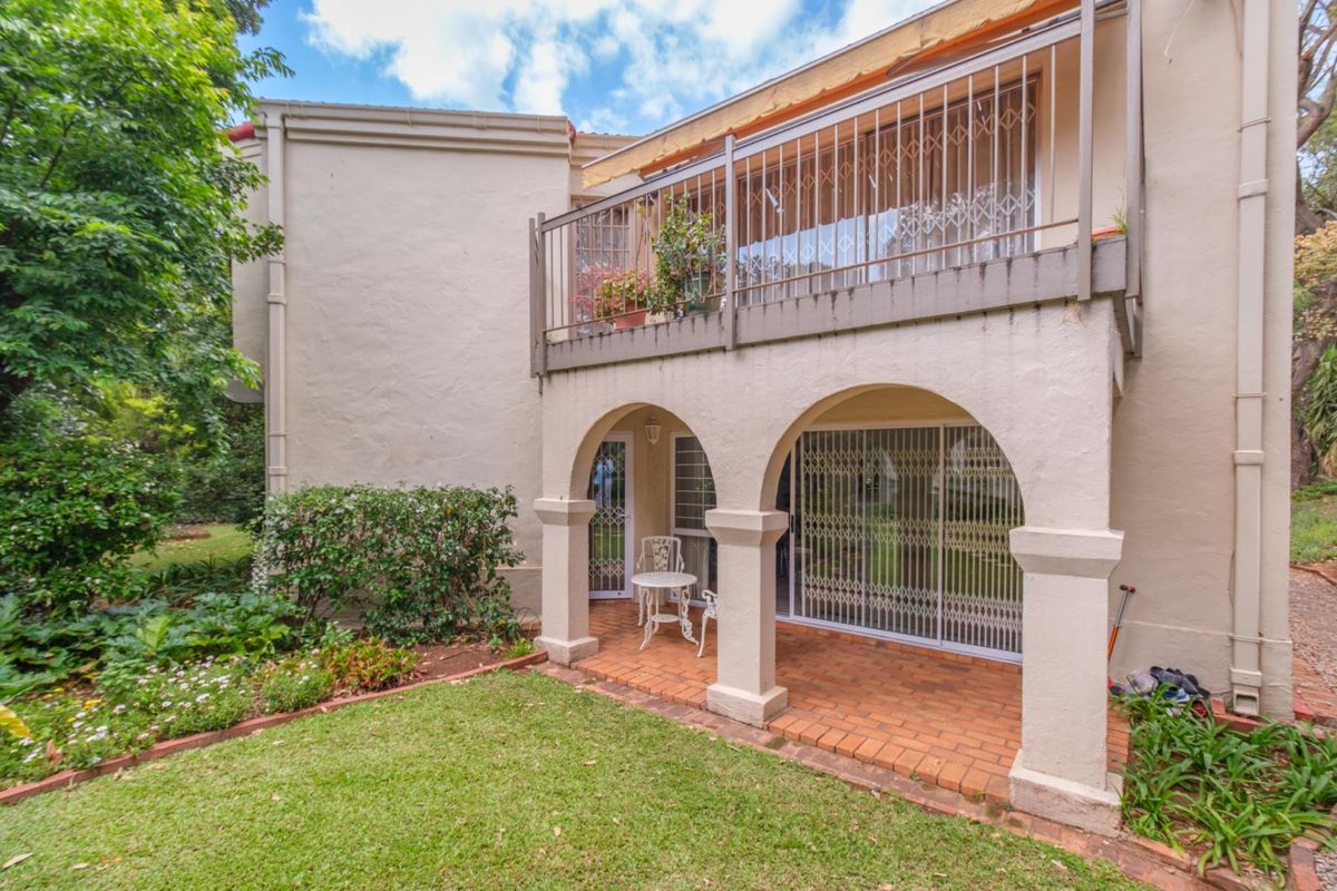 Rear view of the apartment featuring a covered brick patio with arched columns and an upper-level balcony with metal security railings.