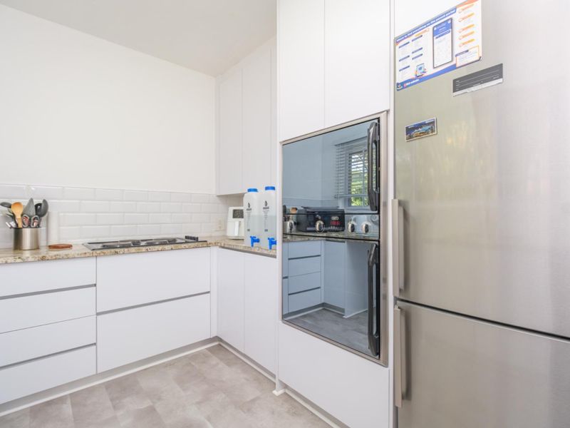 Modern kitchen featuring white cabinetry, granite countertops, subway tile backsplash, and integrated oven with gas hob.