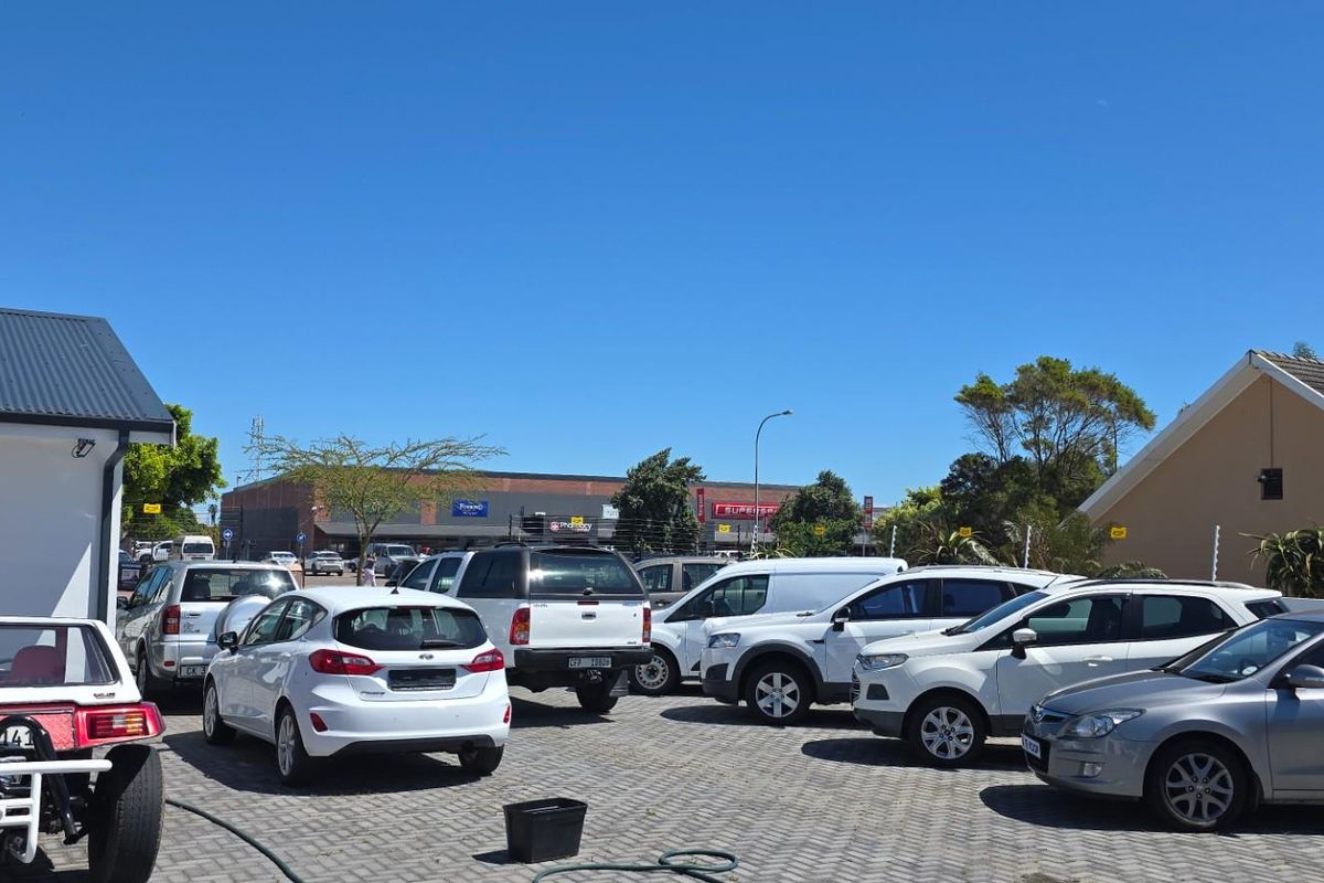 An outdoor paved parking area situated between commercial building structures under a clear blue sky.
