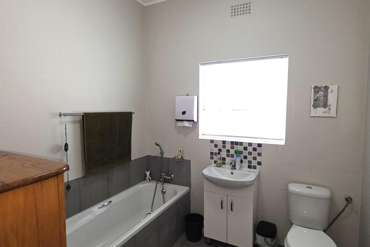 A functional bathroom featuring a bathtub with handheld shower, vanity basin, and toilet, finished with neutral wall paint and tiled splashback areas.