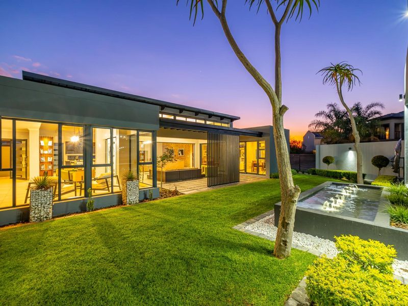A beautifully landscaped rear garden featuring a modern water feature, manicured lawn, and seamless indoor-outdoor flow through large glass sliding doors.