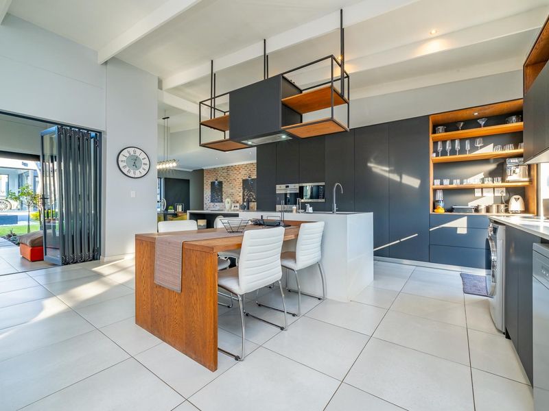 Modern open-plan kitchen featuring sleek dark cabinetry, a central island with integrated dining, exposed ceiling beams, and seamless access to the outdoor patio area.