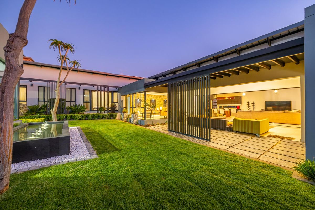 A beautifully landscaped rear garden featuring a modern water feature, paved patio area, and seamless indoor-outdoor flow through large sliding doors into the living space.