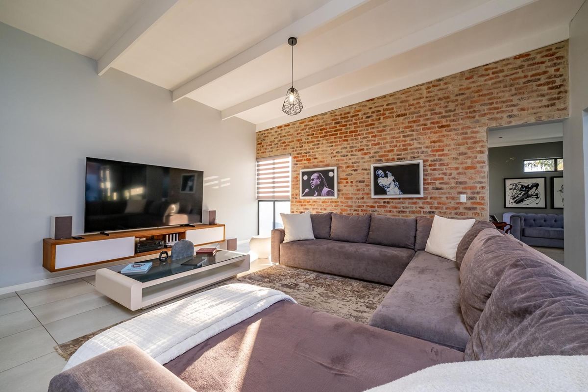 Spacious living room featuring an exposed brick feature wall, high ceilings with exposed beams, and modern tiled flooring.