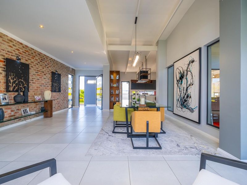 Spacious open-plan living and dining area featuring a striking exposed brick feature wall, modern tiled flooring, and elegant pendant lighting.