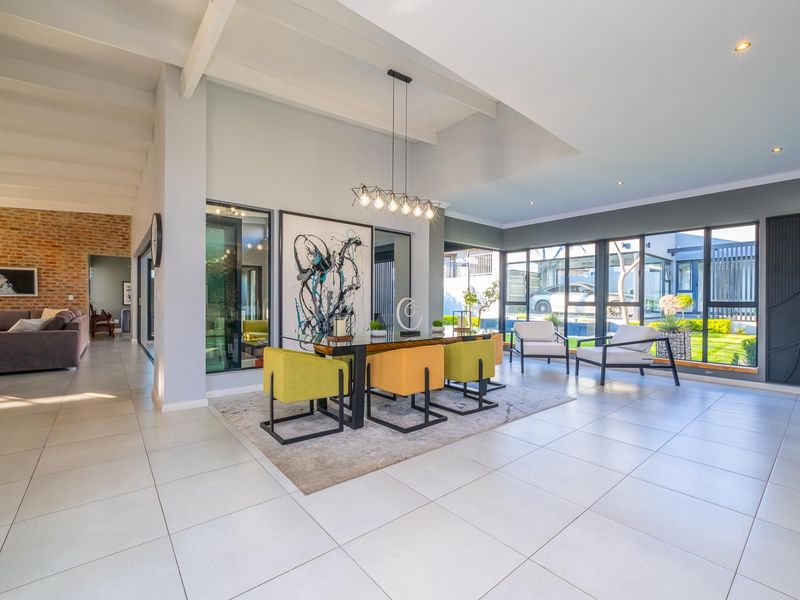 Spacious open-plan living and dining area featuring large windows, exposed brick accents, tiled floors, and exposed ceiling beams with modern lighting.