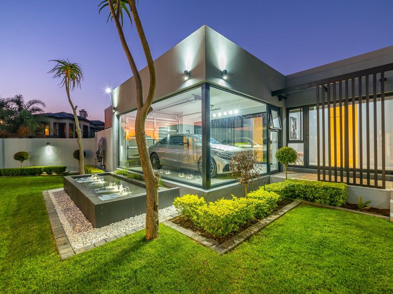 Modern glass-walled garage featuring a sleek design, integrated water feature, and beautifully landscaped garden, creating a sophisticated architectural aesthetic.