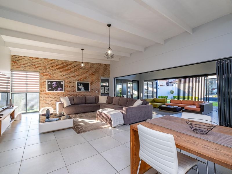 Spacious open-plan living and dining area featuring an exposed brick wall, high exposed beam ceilings, and large stacking doors opening to the patio.