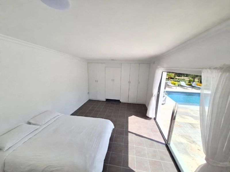 Spacious bedroom featuring built-in cupboards, tiled flooring, and a large sliding glass door providing direct access to the pool area.