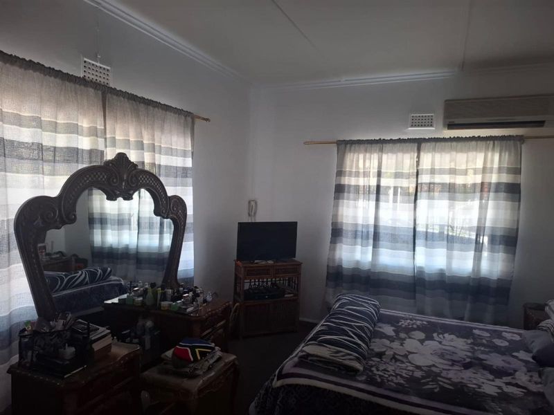 A bedroom featuring white walls, dual windows with curtain rods, and a wall-mounted air conditioning unit.
