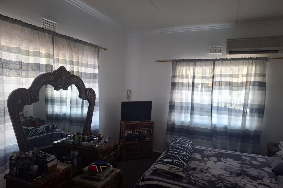 A bedroom featuring white walls, dual windows with curtain rods, and a wall-mounted air conditioning unit.