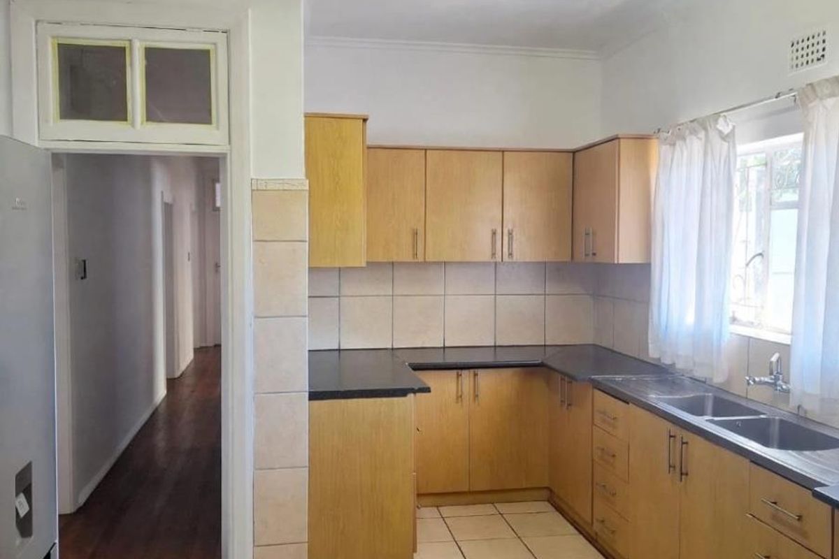 A functional kitchen featuring laminate cabinetry, dark countertops, double stainless steel sink, and ceramic tiled flooring with direct access to the hallway.
