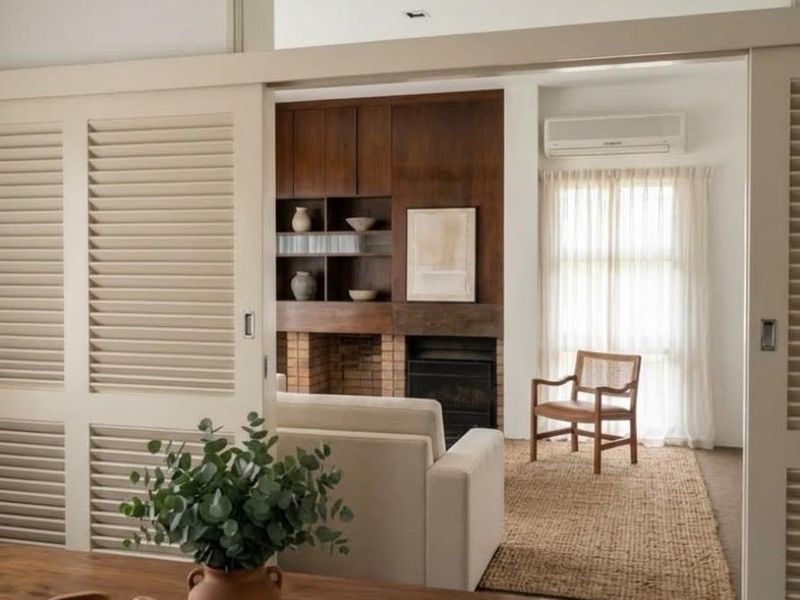 A well-appointed living room featuring a brick fireplace, custom built-in wooden cabinetry, and elegant sliding louvered doors, creating a warm and inviting atmosphere.