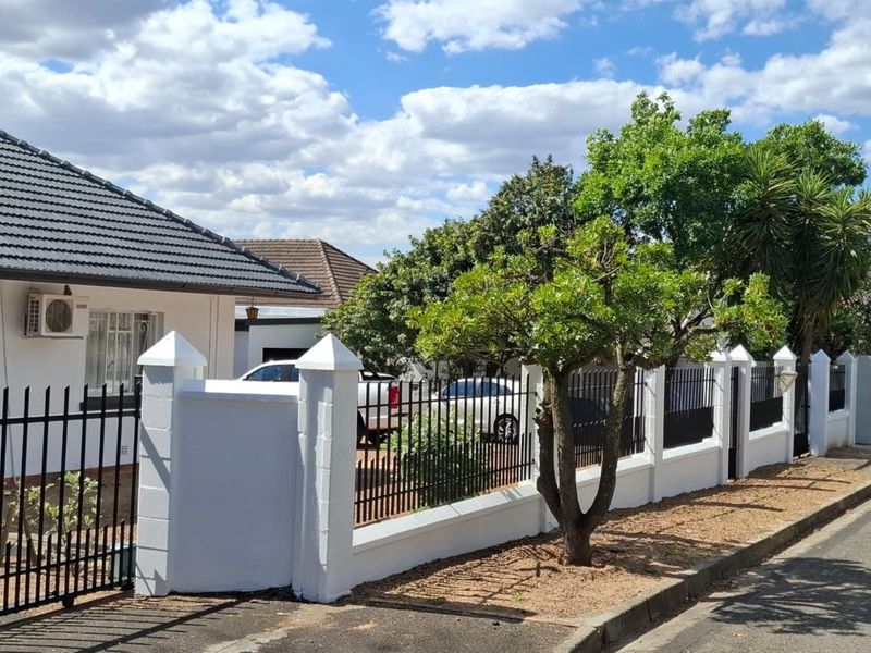 Front exterior view of the property featuring a white perimeter wall with metal fencing, tiled roof, and a wall-mounted air conditioning unit.