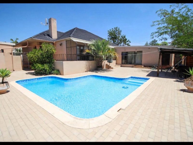 A well-maintained outdoor pool area featuring a paved patio, swimming pool, and rear building elevation with a chimney.