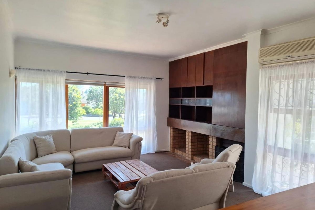Spacious living room featuring a brick fireplace, extensive built-in wooden cabinetry, and large windows providing natural light and garden views.