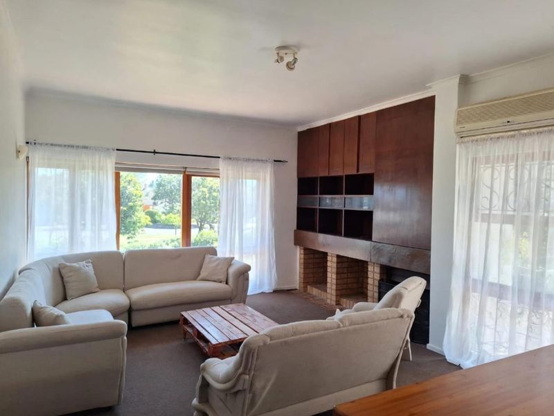 Spacious living room featuring a brick fireplace, extensive built-in wooden cabinetry, and large windows providing natural light and garden views.