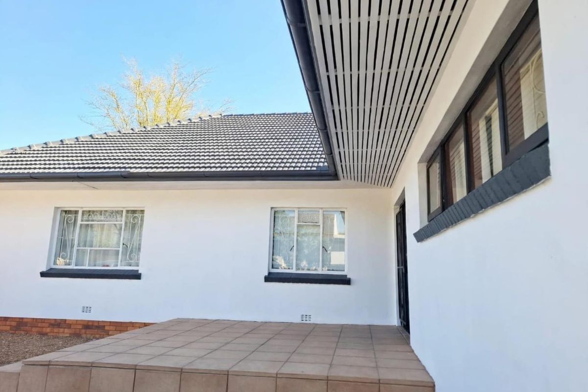 A well-maintained rear exterior view featuring a tiled patio, clean white facade, and modern slatted eaves under a tiled roof.