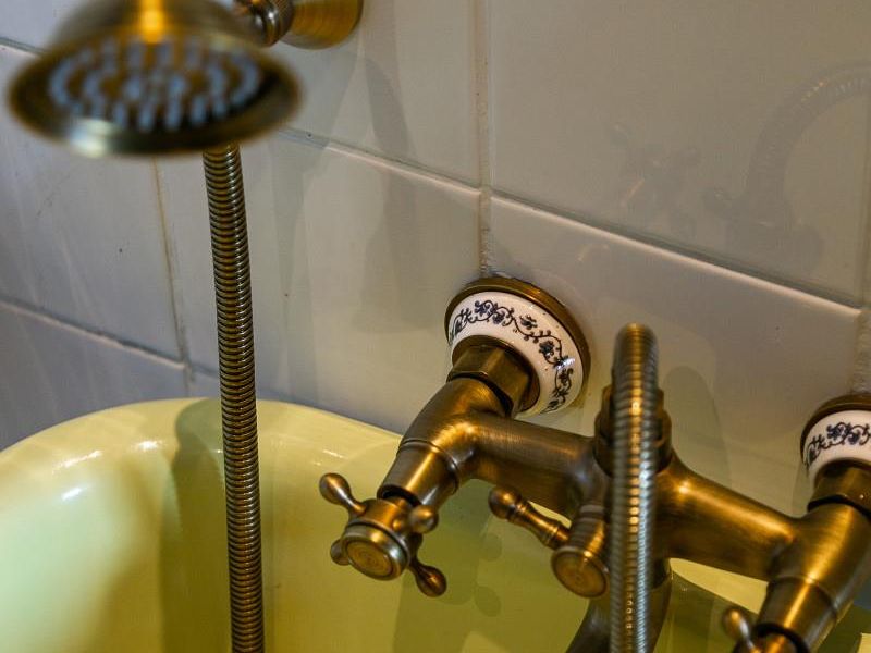 Close-up view of a vintage-style brass bathtub faucet and handheld shower fixture set against white ceramic wall tiles.