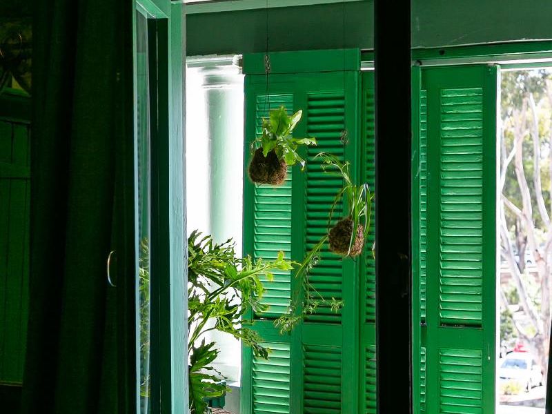 A charming balcony featuring vibrant green louvred shutters, a classic balustrade, and decorative stained glass transom windows overlooking the exterior.