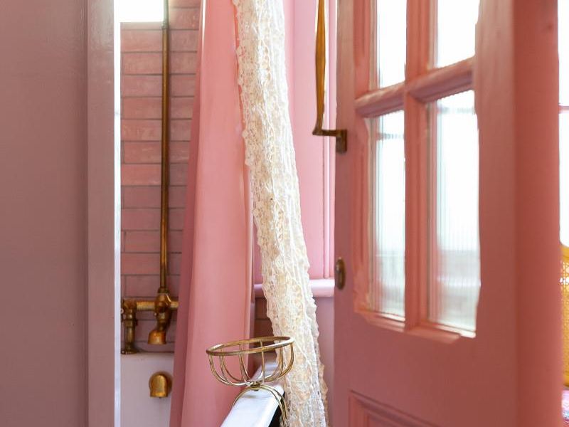 A charming bathroom featuring a classic clawfoot bathtub with brass fixtures, set against pink tiled walls and accessed through a glass-paneled door.