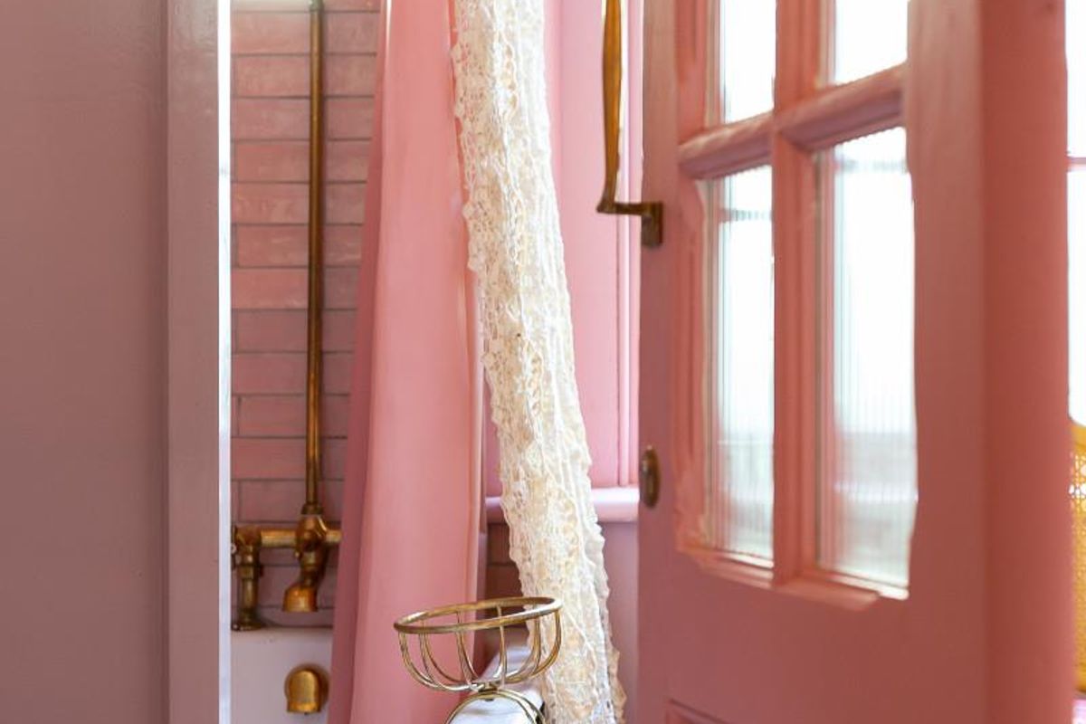 A charming bathroom featuring a classic clawfoot bathtub with brass fixtures, set against pink tiled walls and accessed through a glass-paneled door.