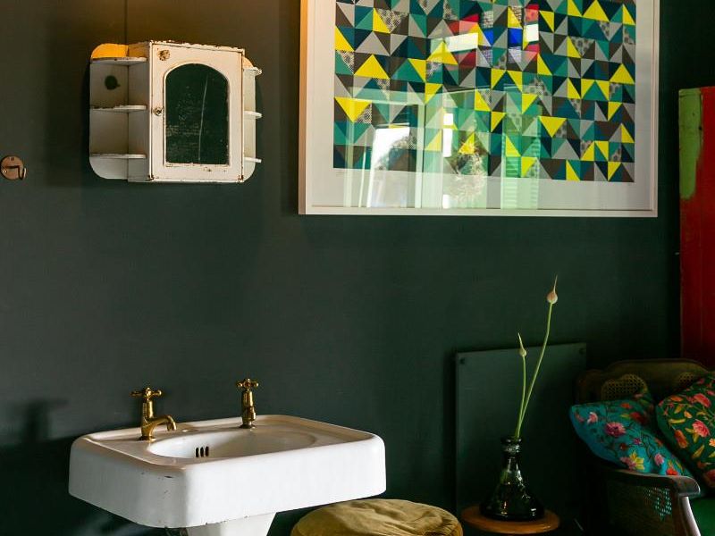 A bathroom area featuring a classic white pedestal sink with brass fixtures and a wall-mounted medicine cabinet against a dark painted wall.