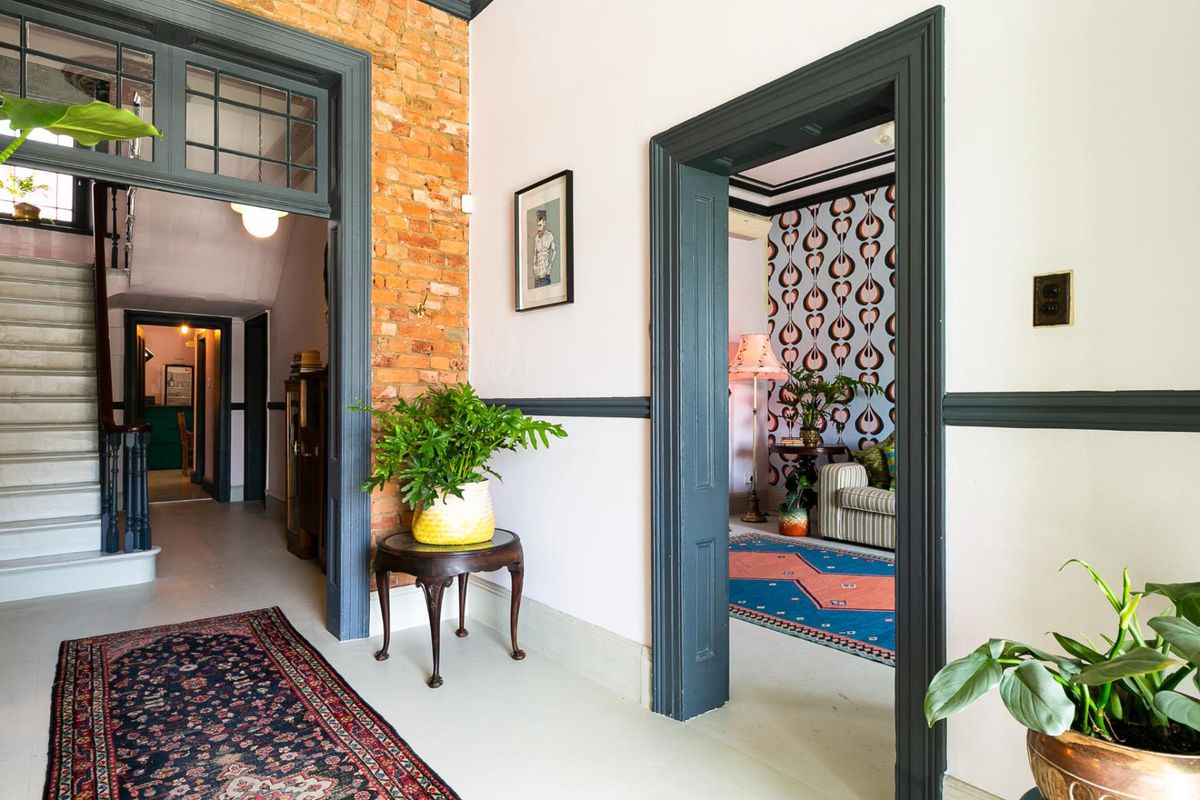 A well-maintained hallway featuring exposed brickwork, classic timber door frames, and a staircase leading to the upper level.