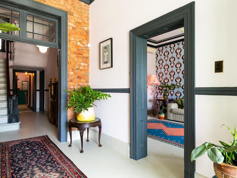 A well-maintained hallway featuring exposed brickwork, classic timber door frames, and a staircase leading to the upper level.