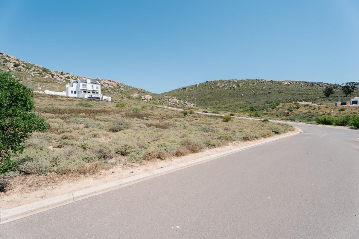 A view of the paved street frontage and surrounding sloped, undeveloped residential land with natural vegetation.
