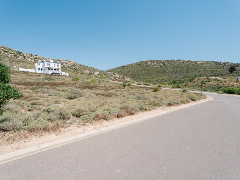 A view of the paved street frontage and surrounding sloped, undeveloped residential land with natural vegetation.