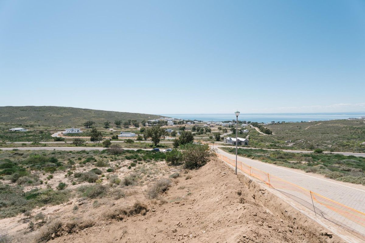 An elevated view of a residential development site featuring a paved road, street lighting, and surrounding coastal landscape.