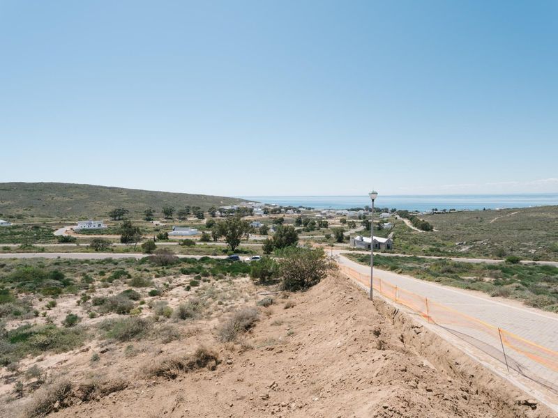 An elevated view of a residential development site featuring a paved road, street lighting, and surrounding coastal landscape.